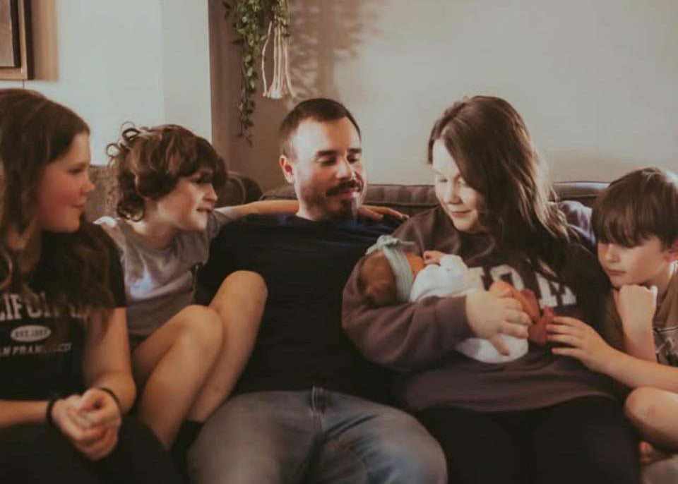 Family of five sitting on a couch with a woman holding a baby.
